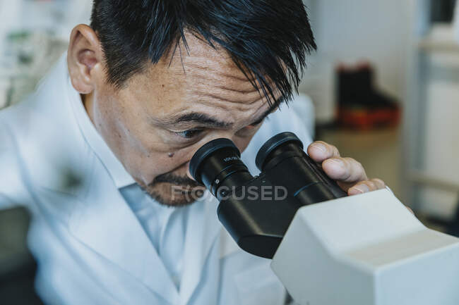Männlicher Wissenschaftler schaut durchs Mikroskop, während Mann im Hintergrund im Labor steht — Stockfoto