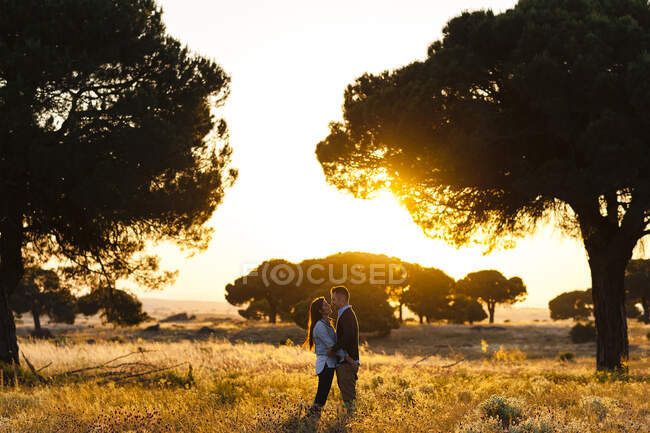 Romantica giovane coppia in piedi sul campo agricolo contro il cielo limpido durante il tramonto — Foto stock