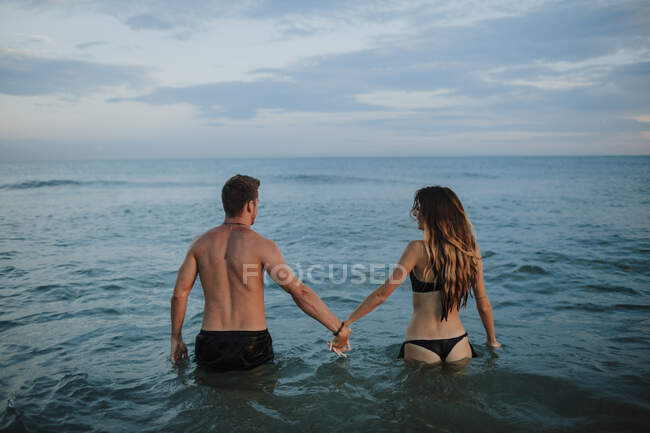 Paar in Badebekleidung hält Hand im Wasser am Strand — Stockfoto