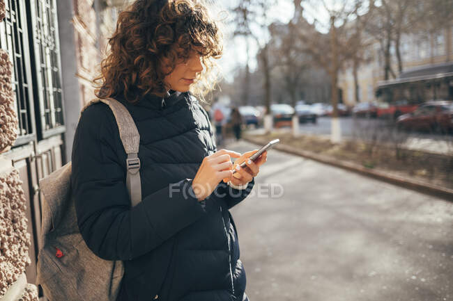 Женщина среднего возраста с сумкой с помощью мобильного телефона, стоя на тротуаре в городе — стоковое фото