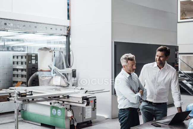 Smiling engineer discussing over laptop with colleague in manufacturing industry — Stock Photo