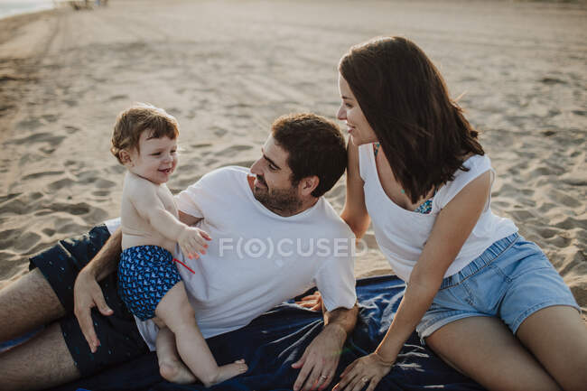 Esposo y esposa pasando tiempo con su hijo en la playa durante el atardecer - foto de stock