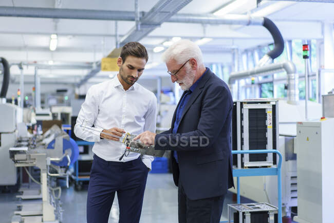 Gerente principal apuntando a la pieza de la máquina mientras discute con el ingeniero por maquinaria en fábrica - foto de stock