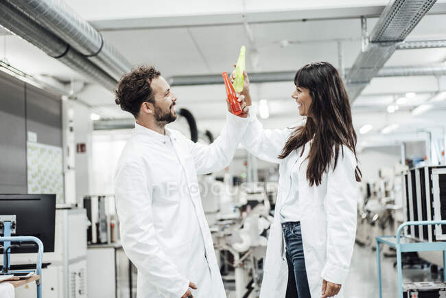Felice tecnici maschi e femmine brindare bevande mentre in piedi in laboratorio — Foto stock