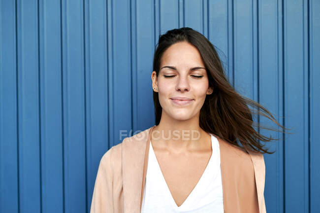 Femme réfléchie avec les yeux fermés debout contre un mur métallique bleu — Photo de stock