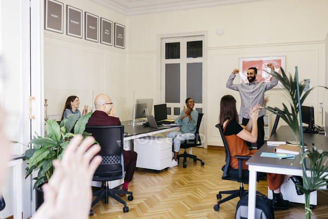 Lächelnder Geschäftsmann jubelt, während Kollegen im Büro klatschen — Stockfoto