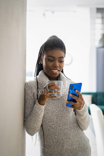 Lächelnde Frau lehnt zu Hause mit Smartphone an Wand — Stockfoto