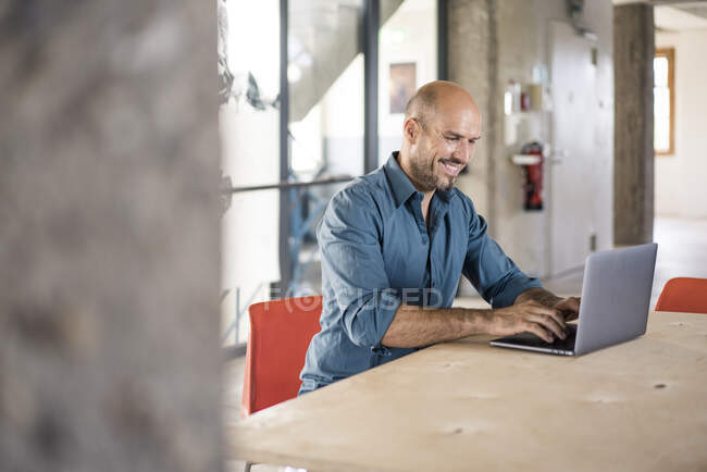 Empresário sorrindo enquanto trabalhava em laptop no escritório — Fotografia de Stock
