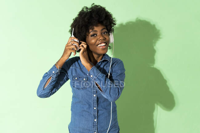 Smiling young woman wearing headphones while standing against green background — Stock Photo