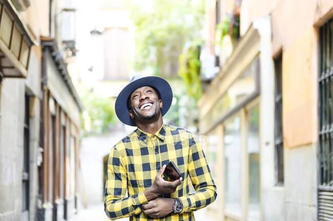 Hombre africano sonriente con teléfono móvil mirando hacia otro lado en la ciudad - foto de stock