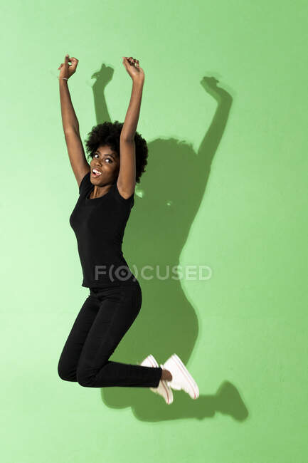 Mujer emocionada saltando con la mano levantada sobre fondo verde - foto de stock