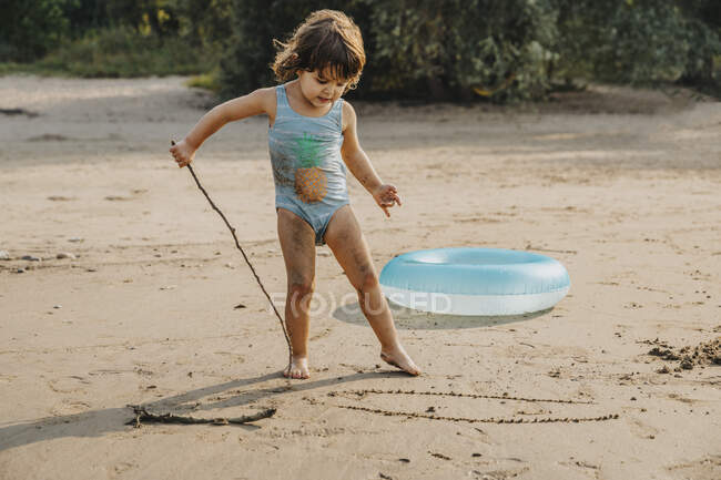 Милая девушка рисует с палкой на песке на пляже — стоковое фото