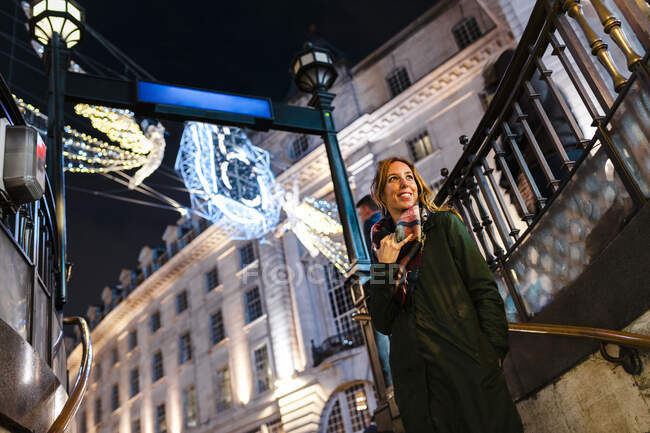 Femme souriante debout sous les lumières de Noël sur Regent Street à Londres, Royaume-Uni — Photo de stock