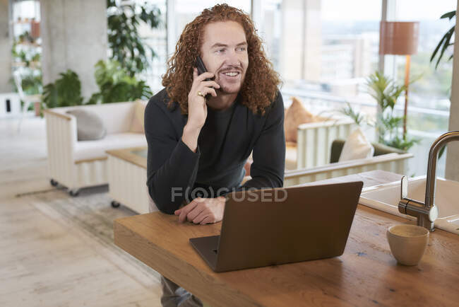 Lächelnder Mann spricht auf Smartphone, während er zu Hause im Wohnzimmer wegschaut — Stockfoto