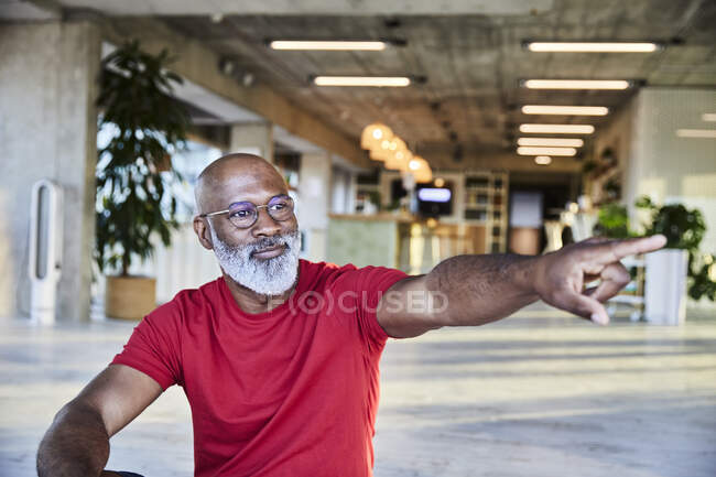 Confident mature man pointing while looking away and sitting at building  terrace — T shirt, mature men - Stock Photo | #481495100