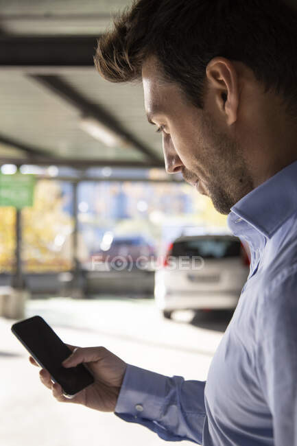 Male entrepreneur using smart phone in parking lot on sunny day — Stock Photo