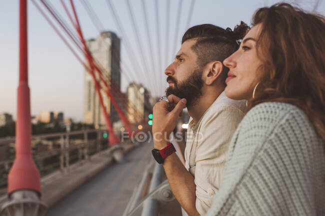 Thoughtful couple looking away while standing on bridge in city — Stock Photo
