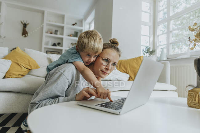 Menino fazendo travessura no laptop enquanto estava atrás da mãe em casa — Fotografia de Stock