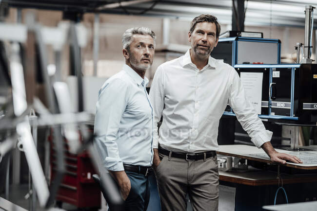 Ingenieros masculinos en formales de pie junto al banco de trabajo en fábrica - foto de stock