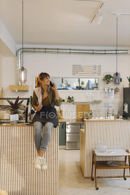 Inhaberin telefoniert mit Smartphone und sitzt in Coffeeshop neben Theke — Stockfoto