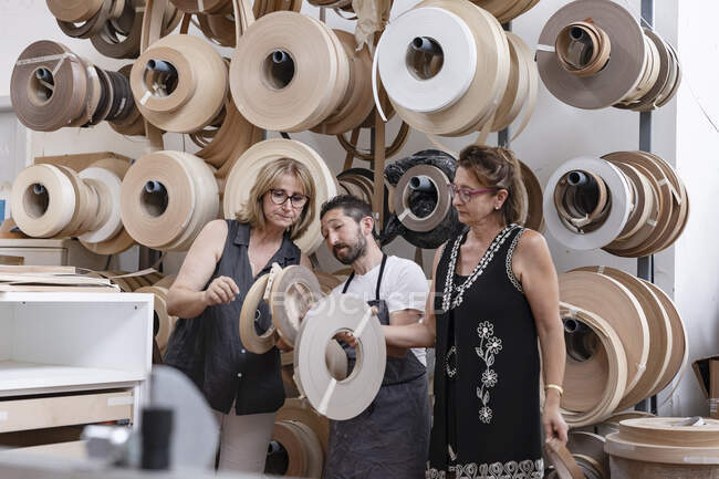 Diseñador de interiores y carpintero eligiendo carrete mientras está parado en el taller - foto de stock