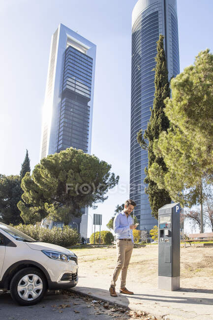 Businessman using mobile phone while standing at parking meter in city - foto de stock