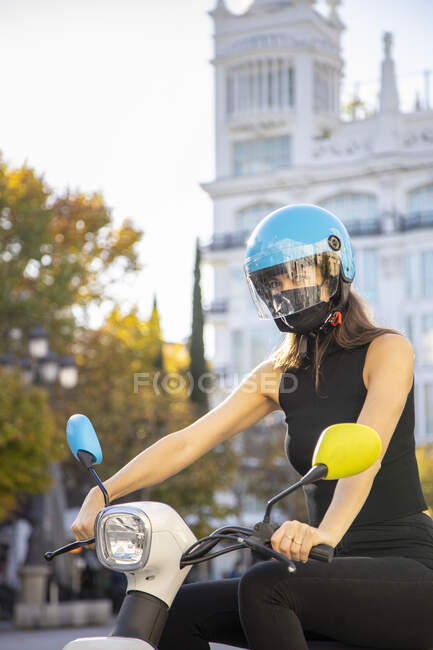 Молодая женщина в маске и шлеме на мотоцикле в городе — стоковое фото