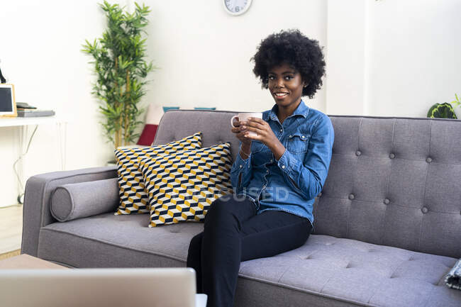 Smiling woman drinking coffee while sitting at home — Stock Photo