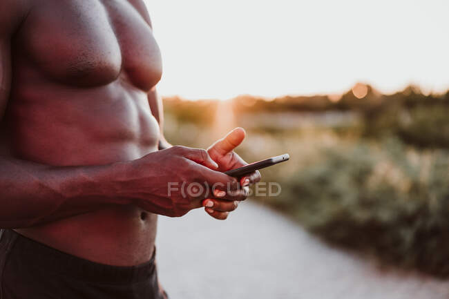 Спортсмен с помощью смартфона стоит в парке на закате — стоковое фото