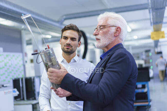 Senior manager discutendo oltre parte della macchina con giovane ingegnere maschio in fabbrica illuminata — Foto stock