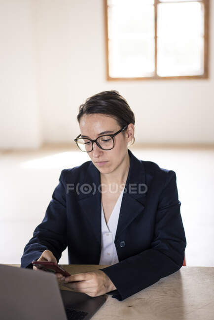 Donna d'affari che utilizza il telefono cellulare mentre siede al tavolo in ufficio — Foto stock
