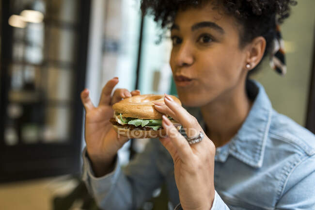 Mitte erwachsene Frau isst Burger, während sie im Café sitzt — Stockfoto