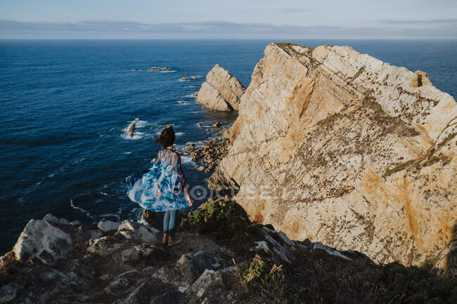 Mitte erwachsene Frau steht auf einem Felsen, während sie im Urlaub aufs Meer schaut — Stockfoto