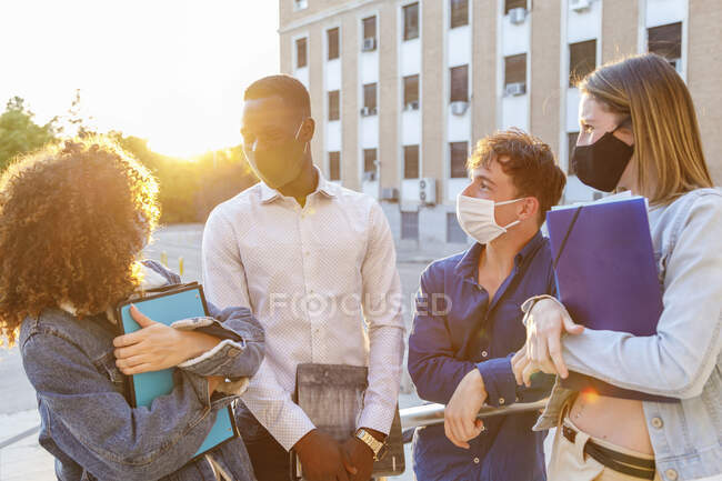 Étudiants masculins et féminins portant un masque de protection lors de discussions sur le campus à l'université — Photo de stock