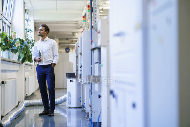 Thoughtful male technician holding digital tablet while looking away at illuminated factory — Stock Photo
