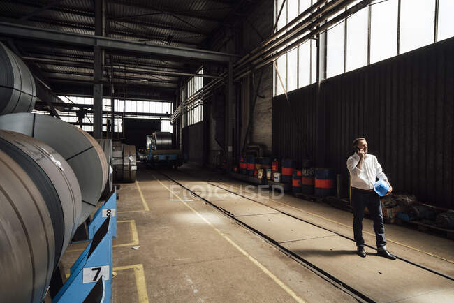 Uomo d'affari che parla su smart phone mentre in piedi in fabbrica — Foto stock