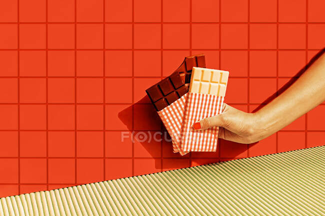 Mano femenina sosteniendo barras de chocolate contra la pared de azulejos rojos - foto de stock