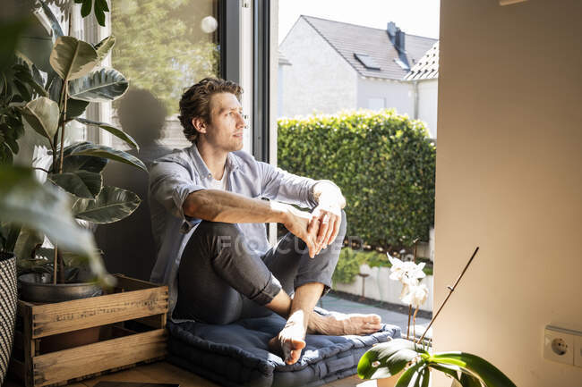 Mittlerer erwachsener Mann sitzt an sonnigen Tagen zu Hause auf einem Kissen — Stockfoto