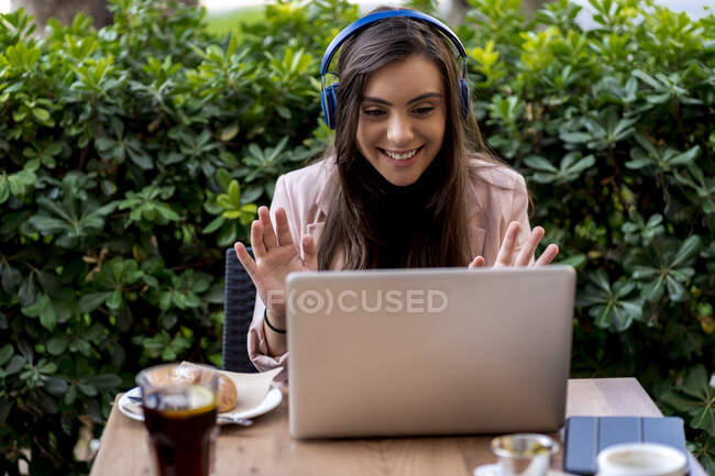 Sourire femme entrepreneur vidéo appelant par ordinateur portable tout en étant assis sur la terrasse au café — Photo de stock