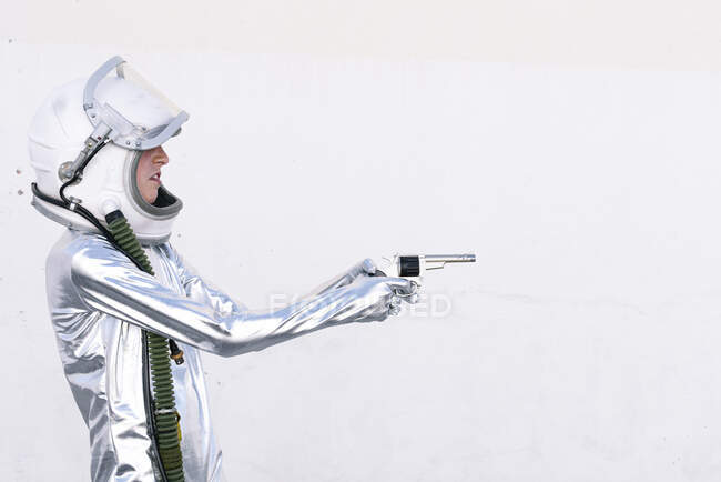 Мальчик в астронавте играет с игрушечным пистолетом, стоя у стены — стоковое фото