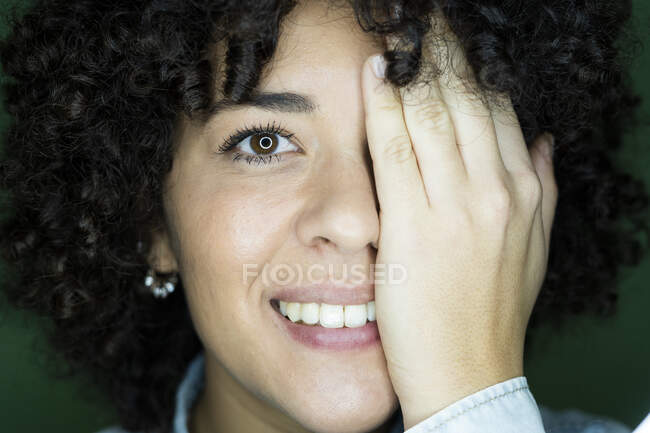Retrato de mujer joven con cabello rizado marrón oscuro que oscurece la cara con la mano - foto de stock