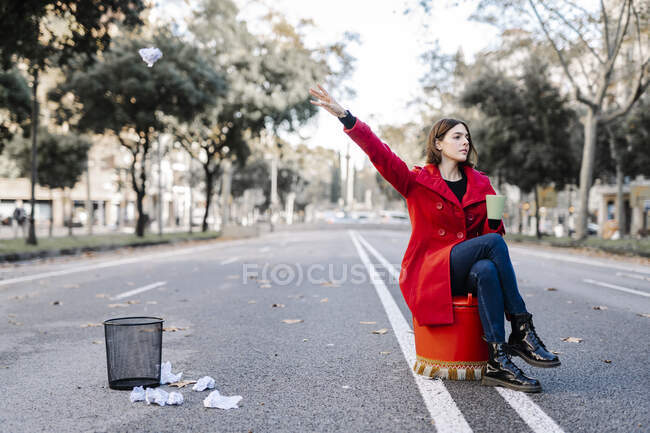 Young woman throwing crumpled paper in garbage can while sitting on street — Stock Photo