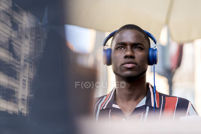 Уверенный молодой человек смотрит в сторону, слушая музыку через наушники в кафе — стоковое фото