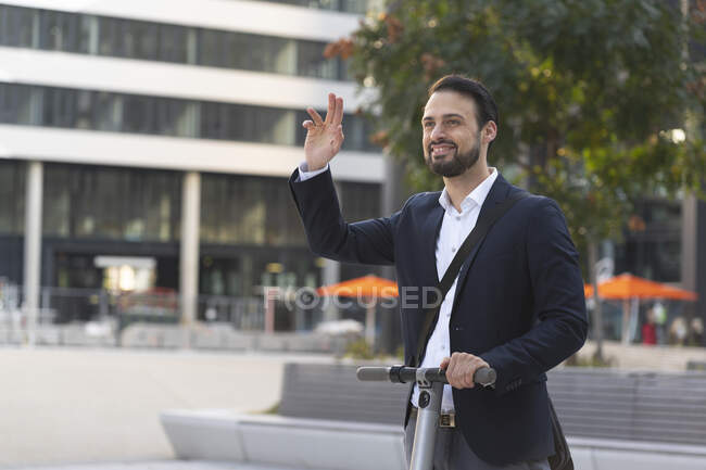 Smiling businessman waving on electric scooter in city — Stock Photo