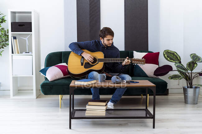 Young musician playing guitar while sitting on sofa at studio — Stock Photo