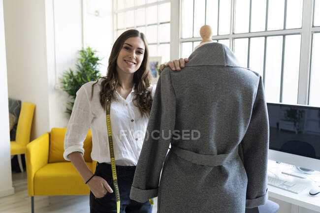 Smiling fashion designer standing by mannequin in studio — Stock Photo