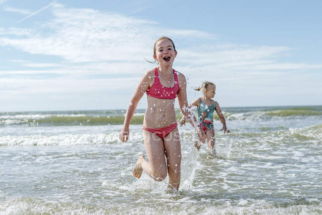 Meninas correndo na água na praia no dia ensolarado — Fotografia de Stock