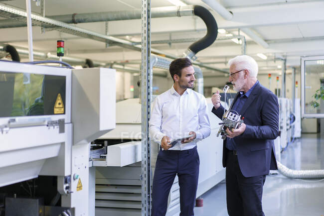 Senior manager discussing machine part with engineer by machinery at factory — Stock Photo