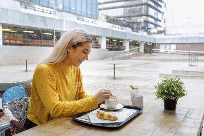 Happy young woman having breakfast at cafe during rainy season — Photo de stock