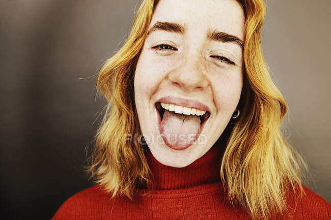 Giocoso adolescente ragazza sporgente lingua mentre in piedi in studio — Foto stock